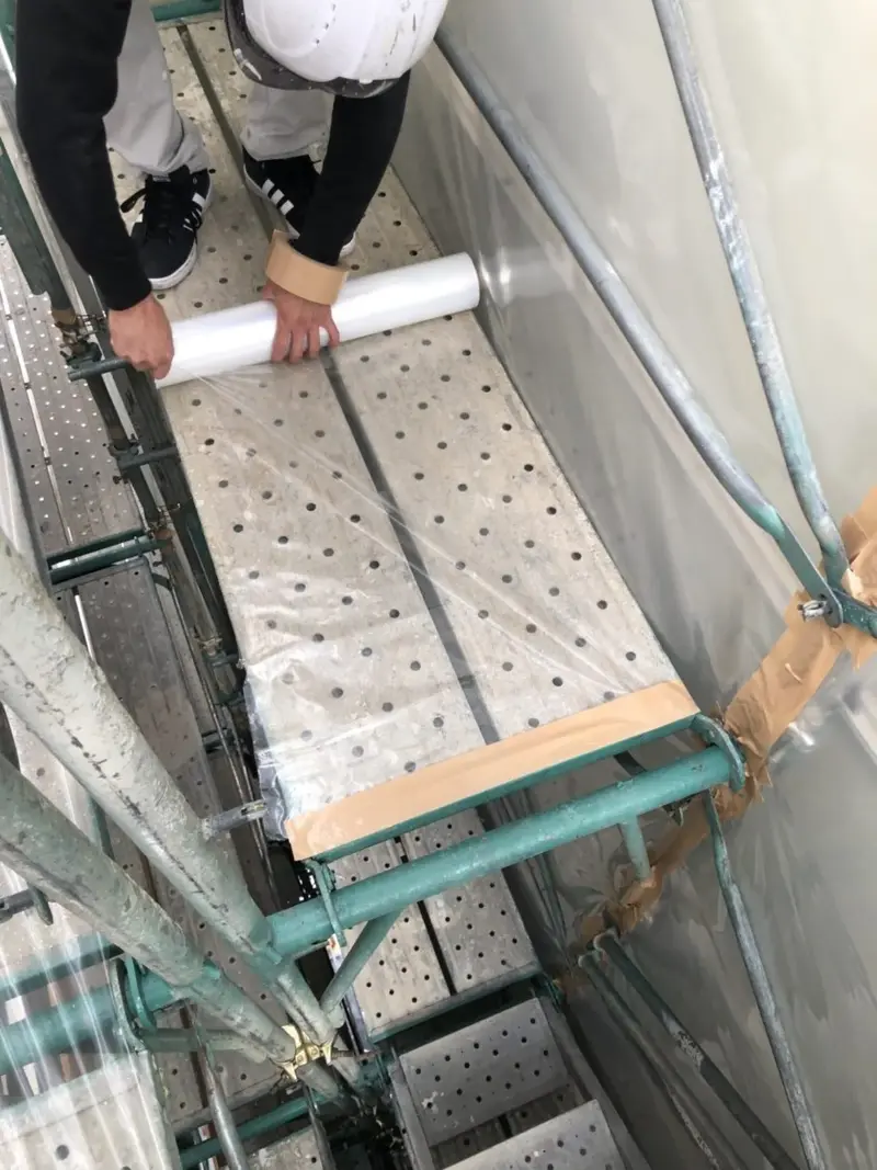 足場の上で養生シートを敷く作業員