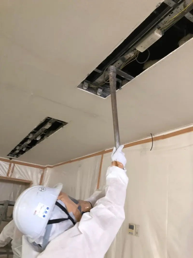 防護服を着用して天井のアスベストを除去する作業員